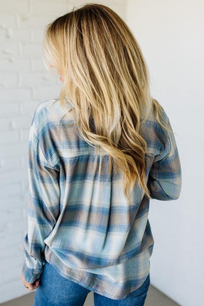 Person wearing a blue and beige plaid shirt against a white wall