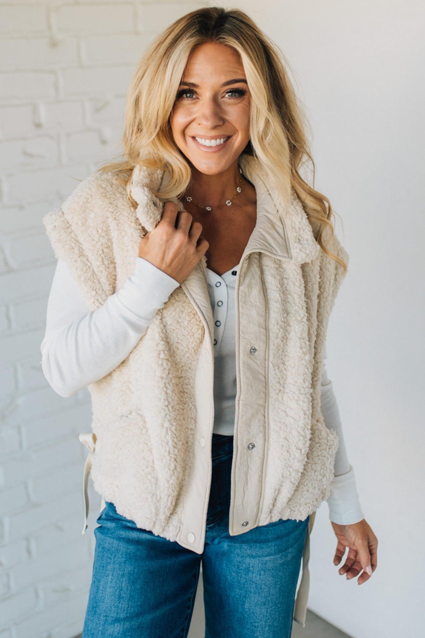 Woman wearing a beige fleece vest against a white brick wall