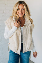 Woman wearing a beige fleece vest against a white brick wall