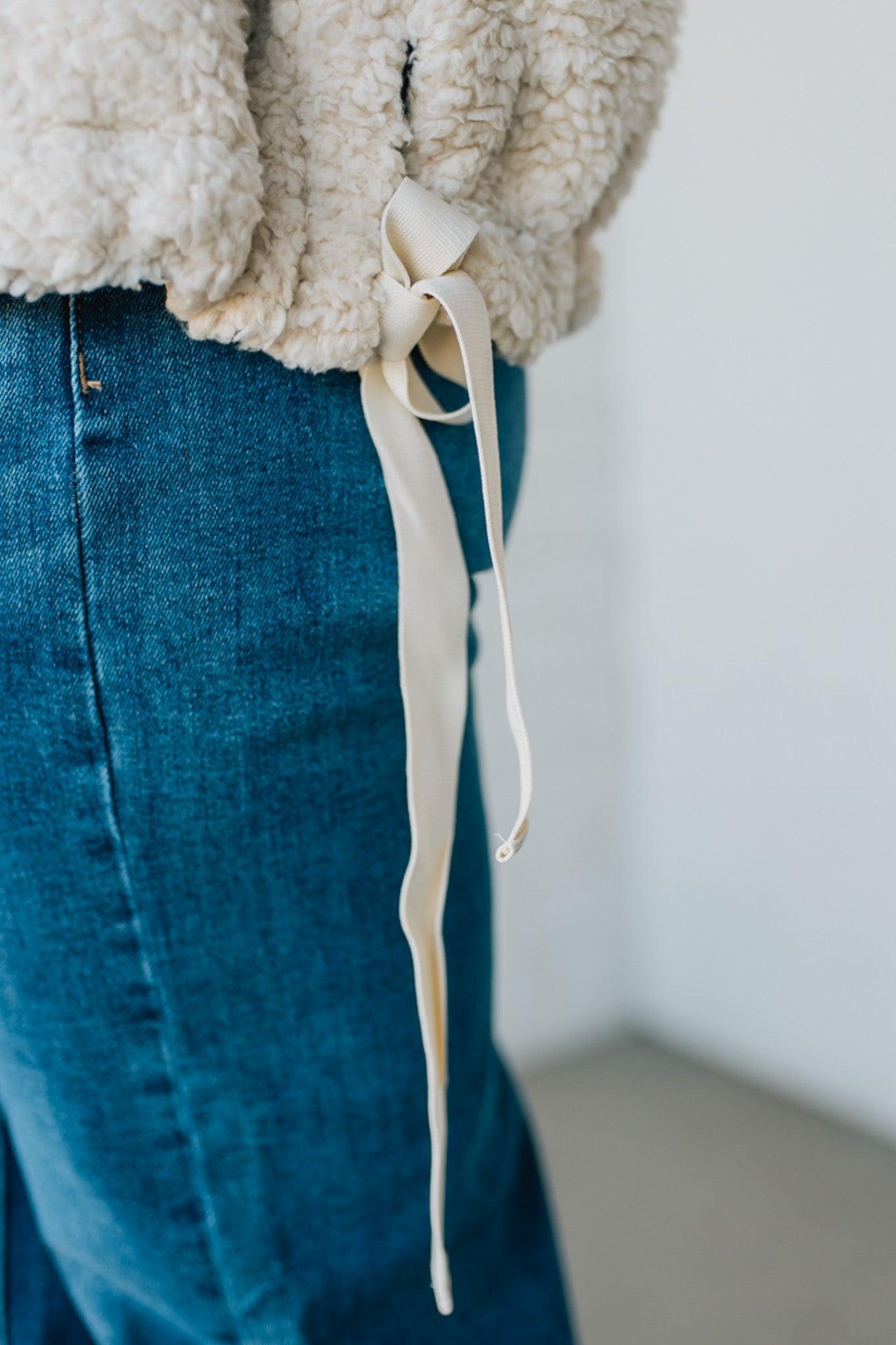 Close-up of a person wearing a beige sherpa jacket and blue jeans with a white background