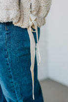 Close-up of a person wearing a beige sherpa jacket and blue jeans with a white background