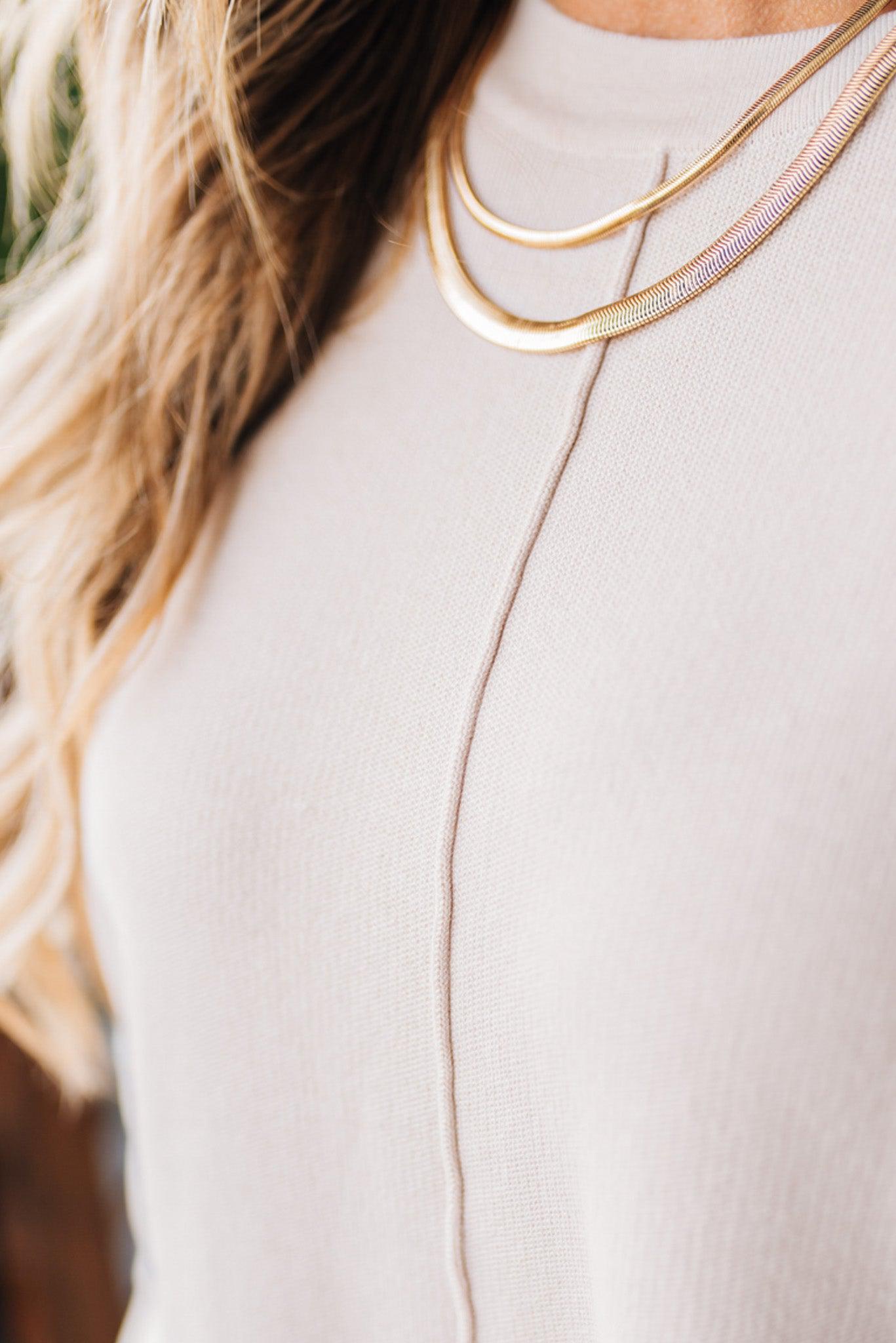 Blonde woman modeling a solid cream colored long sleeve sweater with an oversized fit and seam down the front center