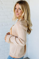 Woman wearing a beige sweater with a white brick wall background