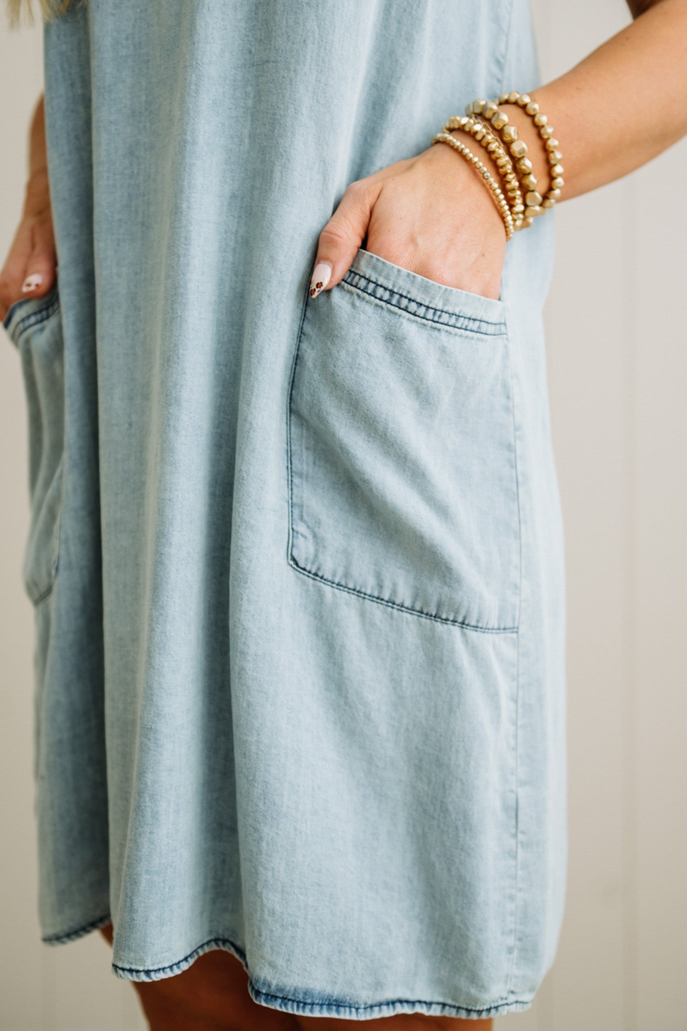 Light blue denim dress with a pocket, worn by a person with gold bracelets.
