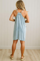 Woman wearing a light blue dress standing against a white paneled wall.