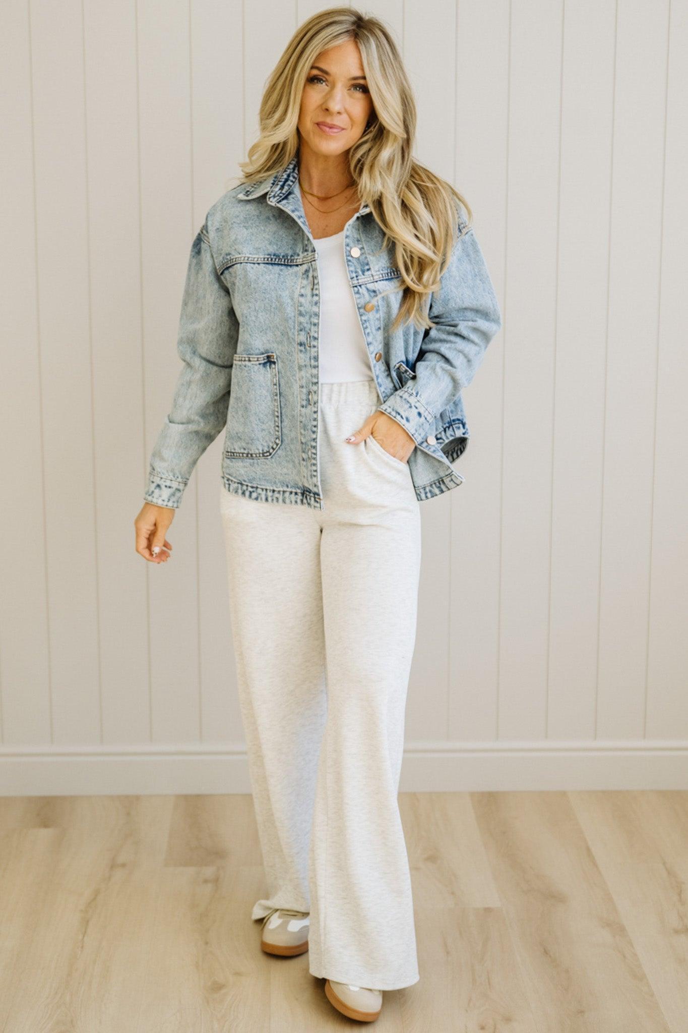 Woman wearing a denim jacket over a white top and pants in a neutral setting