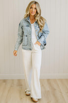 Woman wearing a denim jacket over a white top and pants in a neutral setting