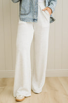 Person wearing white wide-leg pants and a denim jacket against a neutral wall.