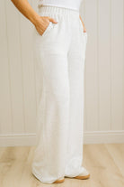 Person wearing white wide-leg pants against a light wooden floor and wall background