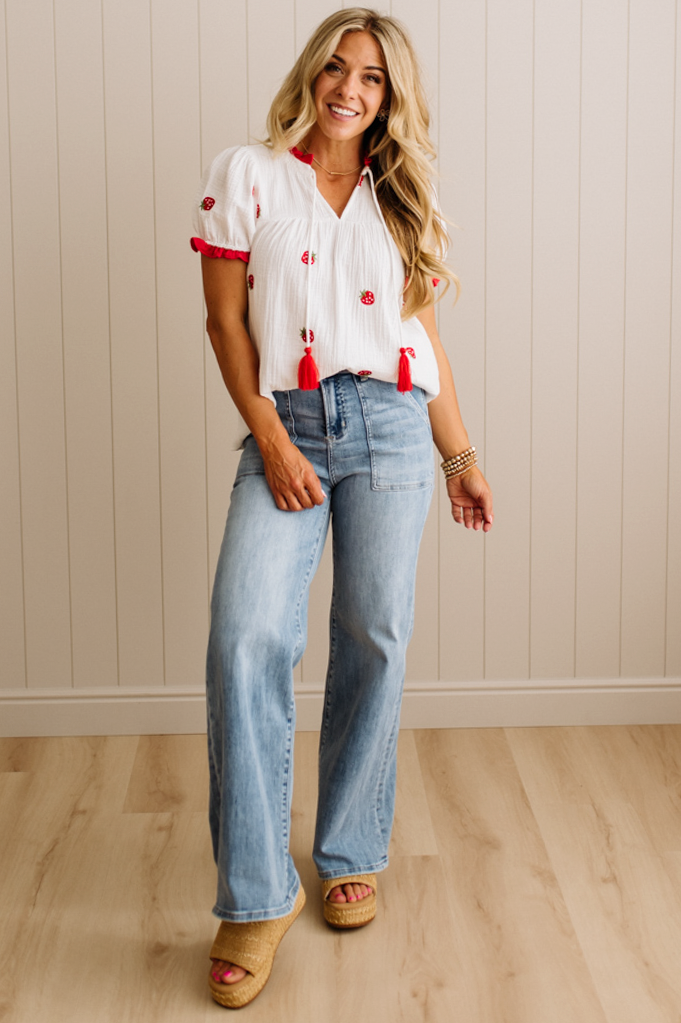 Woman wearing a white blouse with red accents and blue jeans indoors.