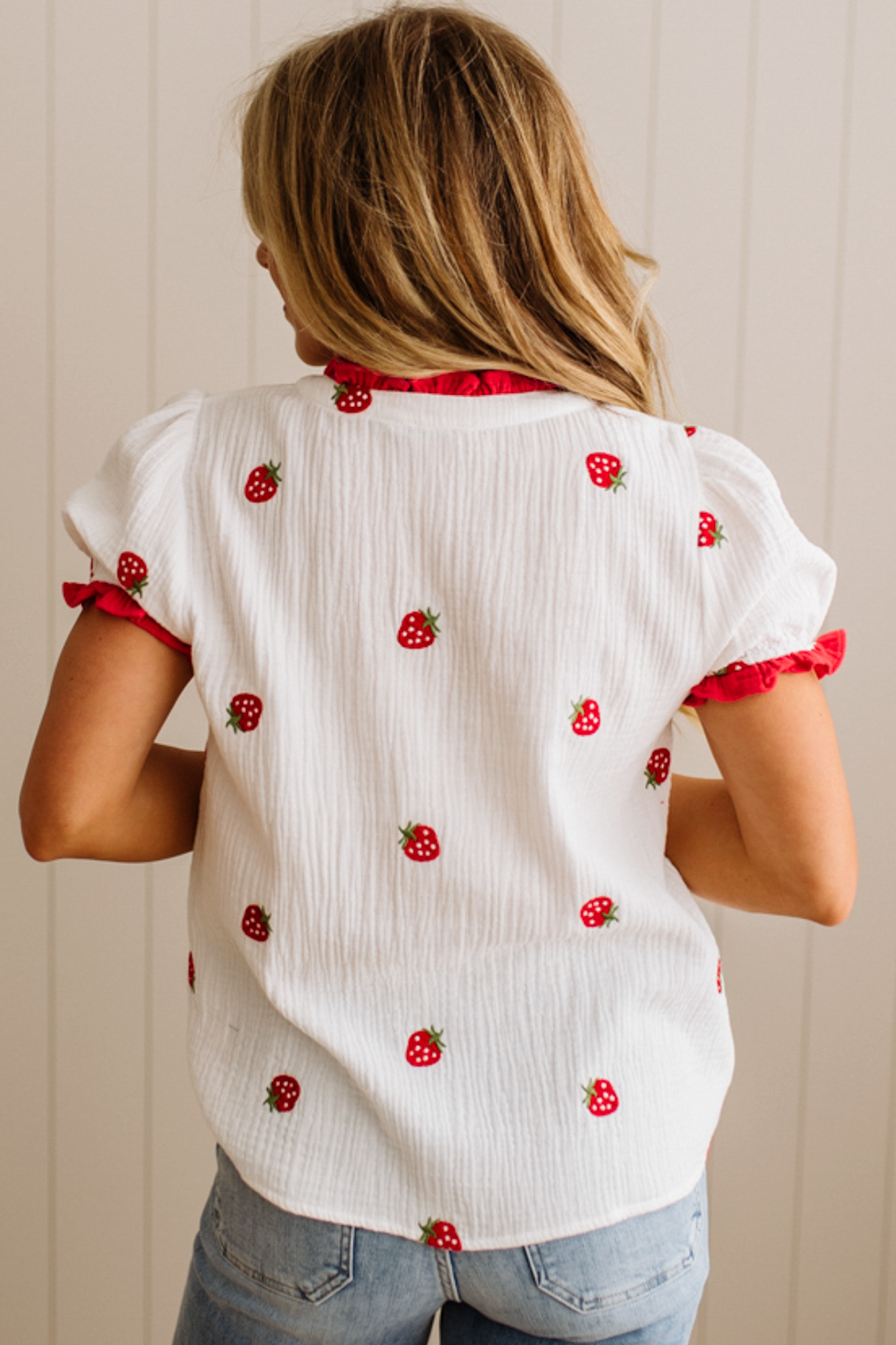 White blouse with red strawberry patterns worn by a person against a neutral background