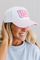 Woman wearing a white cap with pink text and pink visor on a plain background