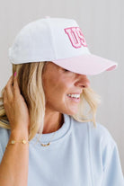 Woman wearing a white cap with pink text on a plain background