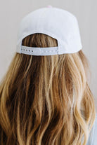 White cap worn by a person with long, wavy hair on a neutral background