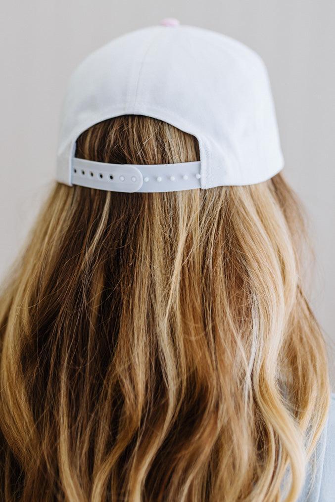 White cap worn by a person with long, wavy hair on a neutral background