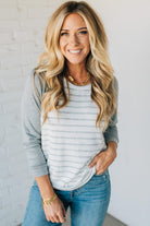 Woman wearing a gray and white striped long-sleeve shirt and blue jeans against a light background