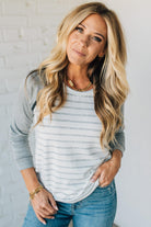Woman wearing a gray and white striped long-sleeve top and blue jeans against a white brick wall.