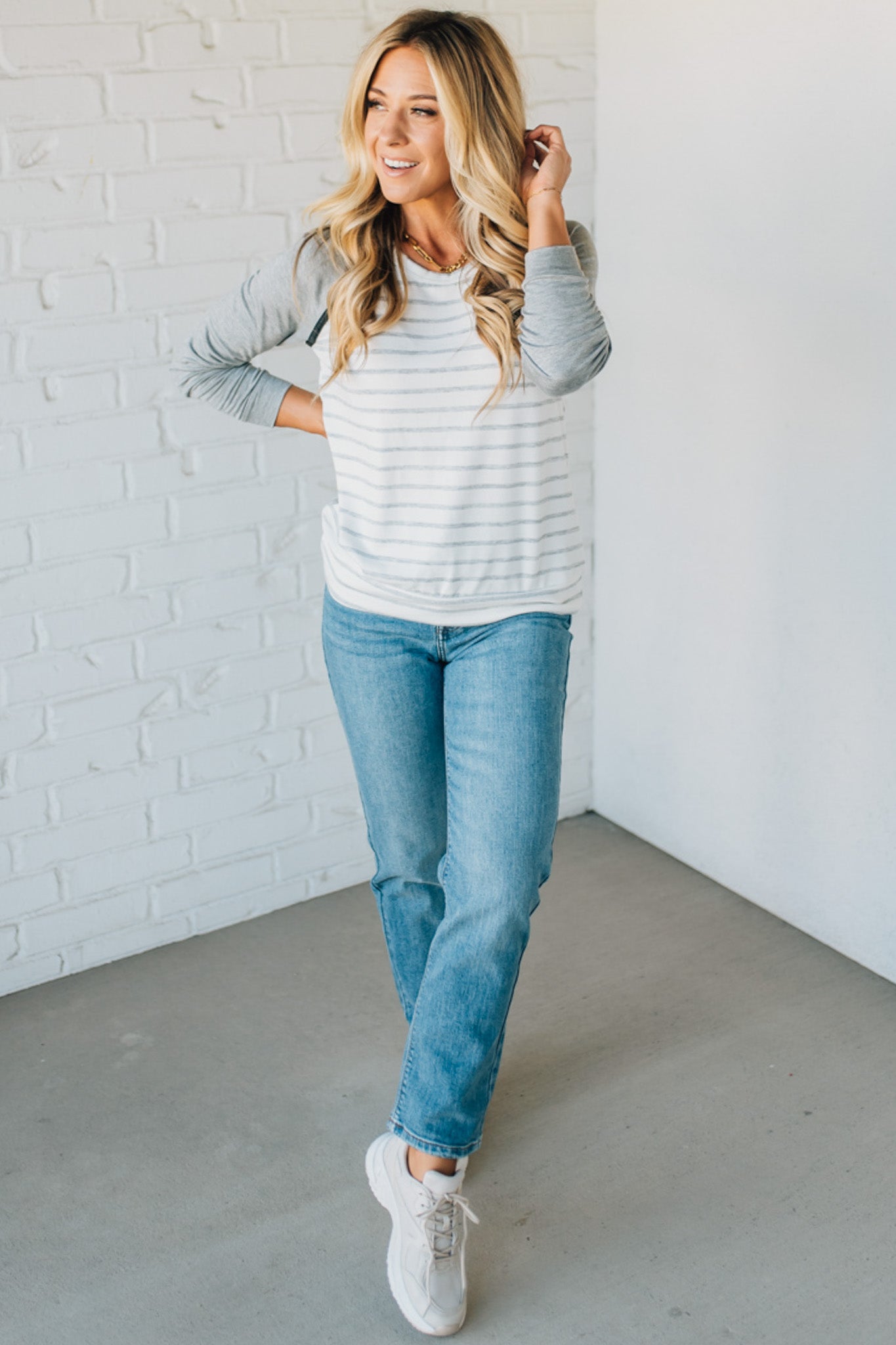 Woman wearing a striped sweater and jeans against a white brick wall.