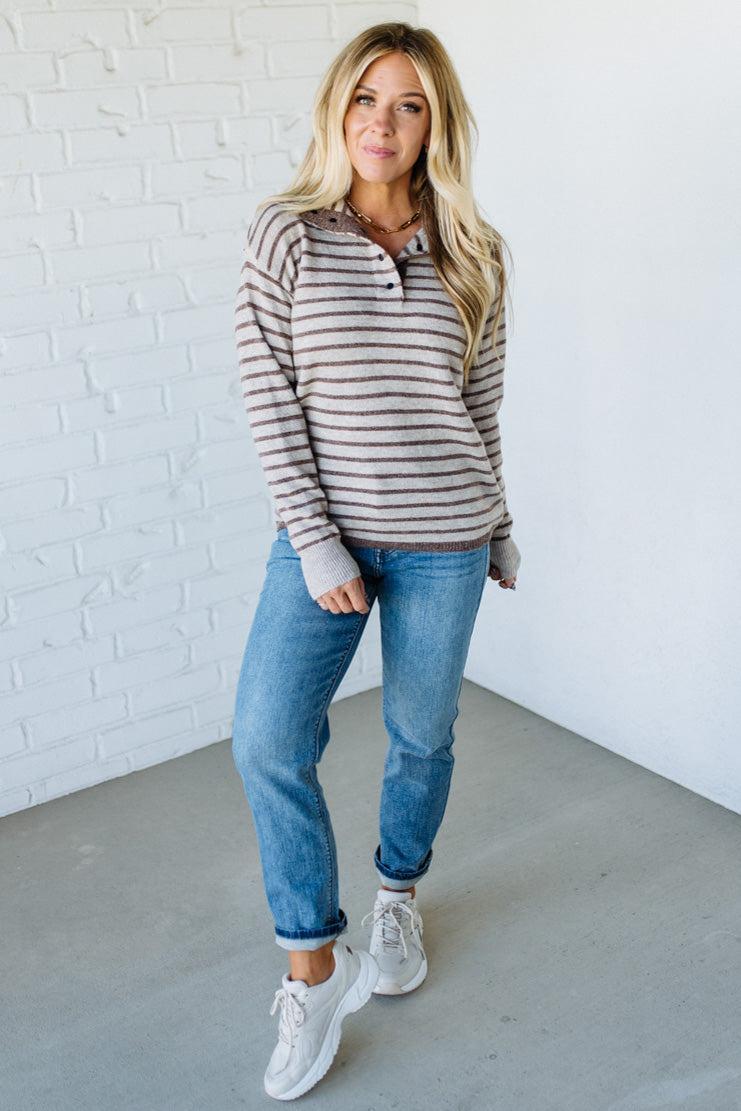 Woman wearing a striped hoodie and jeans standing against a white brick wall.
