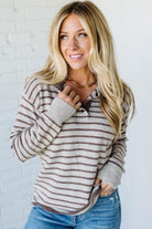 Woman wearing a striped sweater and jeans against a white brick wall.