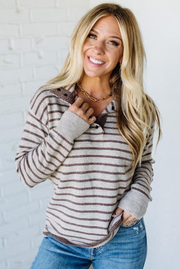 Woman wearing a striped sweater and jeans against a white brick wall