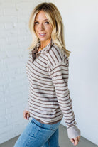 Woman wearing a striped sweater and jeans against a white brick wall.