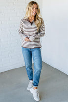 Woman wearing a striped sweater, jeans, and white sneakers against a white brick wall.