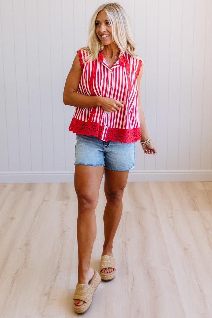 Woman wearing a red and white striped sleeveless top with denim shorts on a light wooden floor.