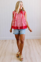 Woman wearing a red and white striped sleeveless top with denim shorts indoors.