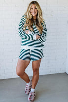 Woman wearing a green and white striped outfit standing against a white brick wall.