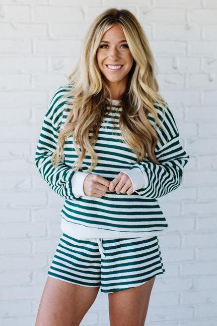 Woman wearing a green and white striped outfit against a white brick wall.