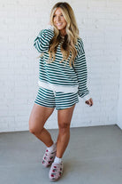 Woman wearing a green and white striped outfit with matching shoes against a white brick wall.