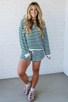 Woman wearing a green and white striped outfit with pink slippers against a white brick wall.