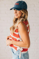 Blonde woman in a hat and shorts wearing a red striped sweater tank with double side ties.