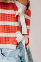 Blonde woman in a hat and shorts wearing a red striped sweater tank with double side ties.