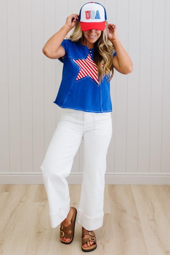 Person wearing a blue top with a red, white, and blue cap and pants indoors.