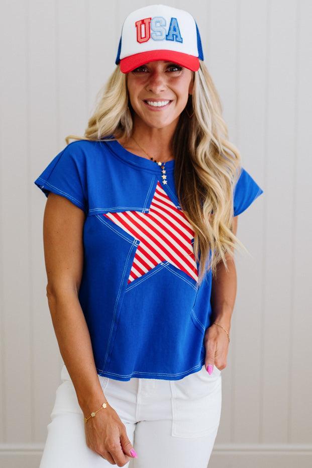 Woman wearing a blue top with an American flag design and a red, white, and blue cap.