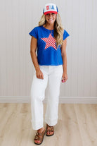 Woman wearing a blue t-shirt with a red, white, and blue star design, white pants, and a matching cap.