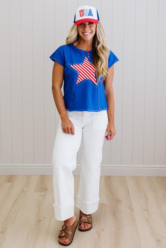 Woman wearing a blue t-shirt with a red, white, and blue star design, white pants, and a matching cap.