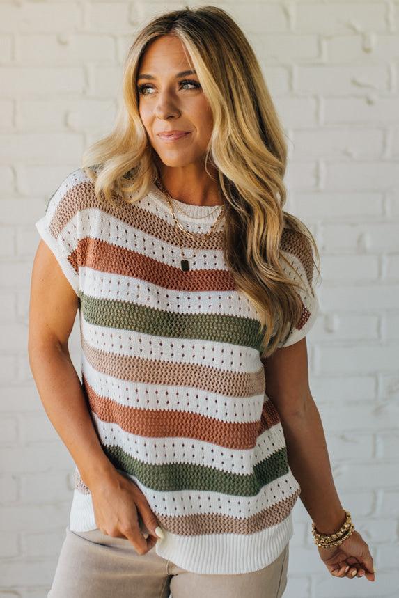 Blonde woman wearing a cream, olive green, mocha and rust striped sweater with jacquard loose weave pattern.