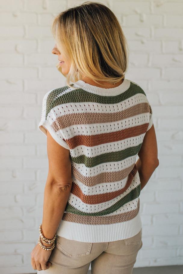 Blonde woman wearing a cream, olive green, mocha and rust striped sweater with jacquard loose weave pattern.