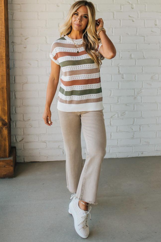 Blonde woman wearing a cream, olive green, mocha and rust striped sweater with jacquard loose weave pattern.