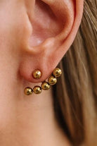 A close-up of a person's ear wearing a cluster of small gold ball stud earrings on the lobe.