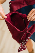 Close-up of a burgundy velvet handbag with silver studs held by a person.
