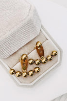 Gold beaded cufflinks displayed on a light beige velvet jewelry box, set against a clean white background.