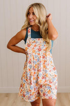 Woman wearing a floral overalls dress against a neutral background