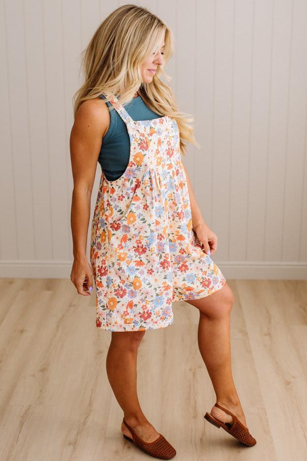 Woman wearing a floral dress over a blue top on a wooden floor.