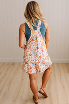 Woman wearing a floral dress over a blue tank top on a wooden floor.