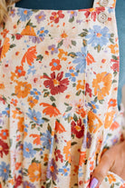 Woman wearing a floral dress over a blue tank top on a wooden floor.