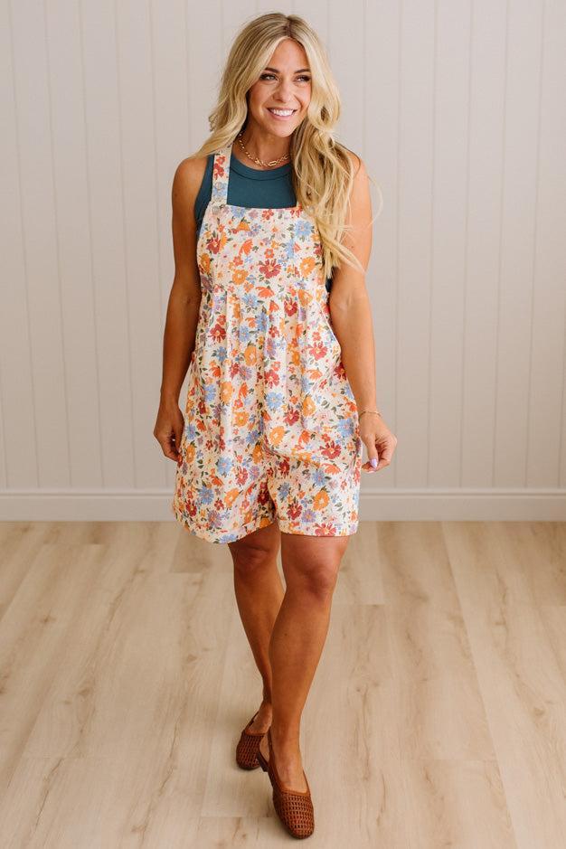 Woman wearing a floral overalls dress against a plain background